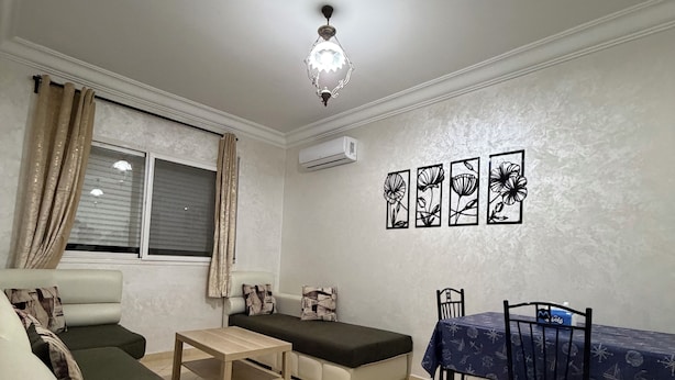 Sala de estar con sofá, mesa de comedor con sillas, una mesita auxiliar, lámpara decorativa y adornos en la pared.