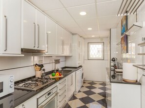 Una cocina moderna con armarios blancos, estufa a gas, microondas y piso a cuadros blanco y negro.