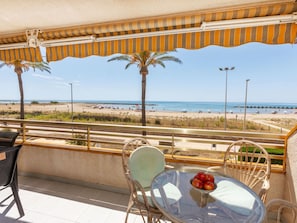 Un balcón con una mesa de vidrio, sillas y vista a la playa.