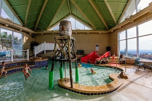 Ein Hallenbad mit Wasserrutsche, Holzkonstruktion und Blick ins Freie.