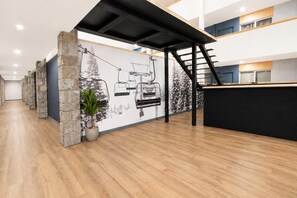 A modern interior with a reception desk, stone pillars, a ski lift mural, and a staircase. - ML 290: Mountain Bliss at Snowshoe | Summer Trails & Breathtaking Views (Snowshoe)