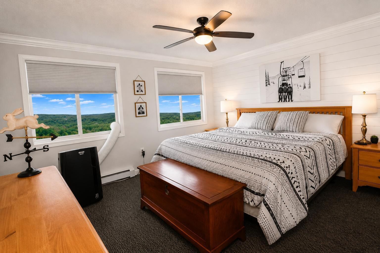 A bedroom with a bed, a desk, a dresser, a ceiling fan, and a window with a view.