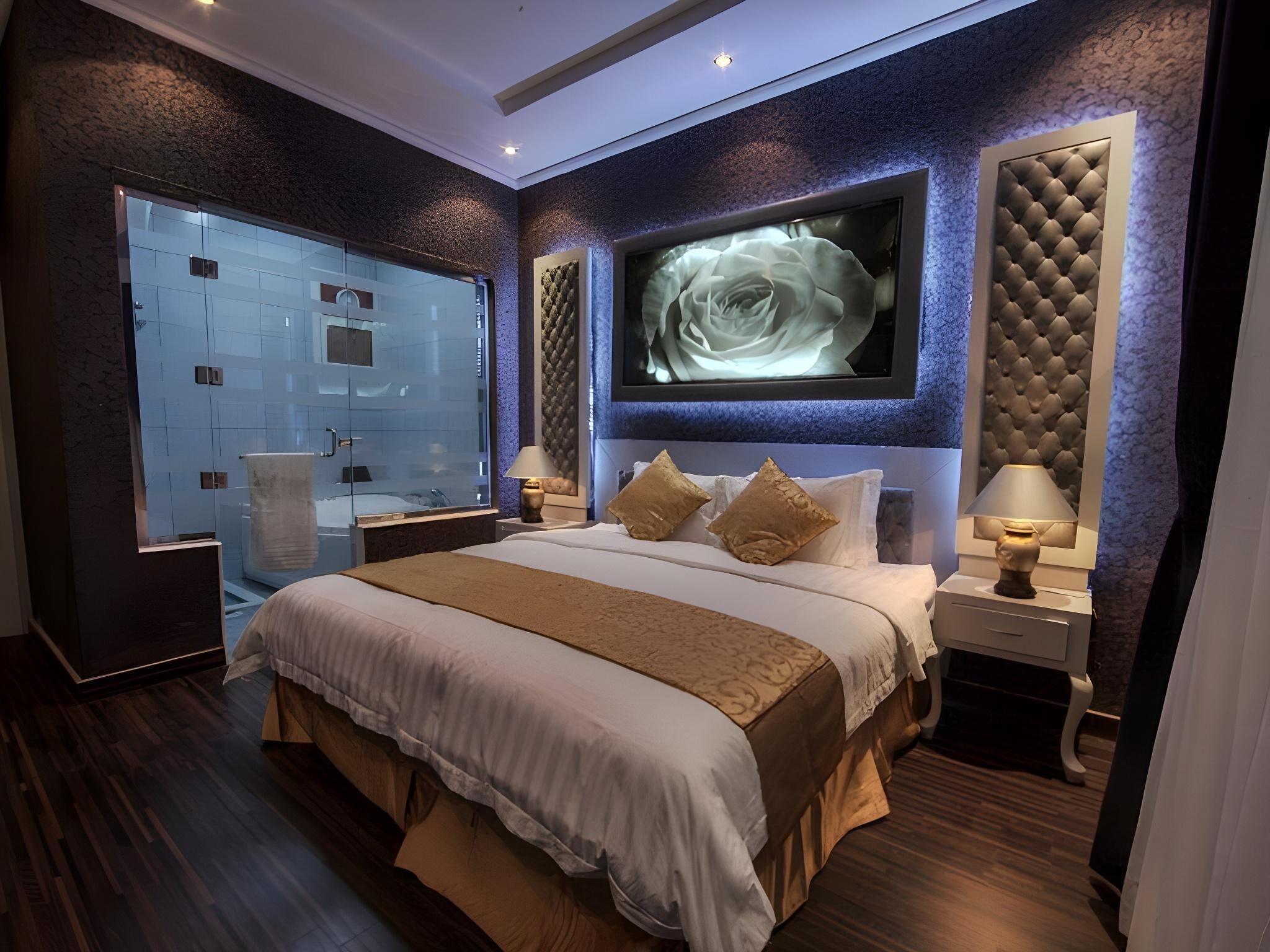 A modern bedroom with a large bed, a glass shower, and a wall-mounted TV.