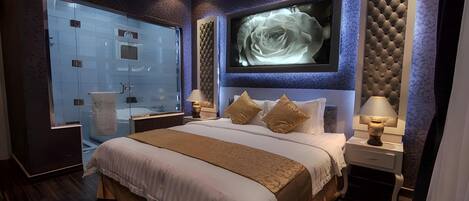 Un dormitorio moderno con una cama grande, ducha de vidrio y televisor montado en la pared.