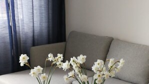 Un salon moderne avec un canapé gris, deux tables en verre avec des pieds en bois et deux vases ornés de fleurs blanches.