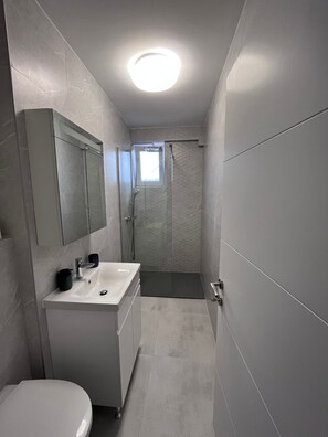 A modern bathroom with a white sink, mirror, and toilet, a shower area, and a skylight. - Charming for 2, Pitesti downtown 1-bedroom 1-bath apartment with AC (Pitești)