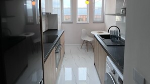 Une cuisine moderne équipée d’un four encastré, d’un évier et d’un lave-vaisselle. On y trouve également un coin repas avec une chaise blanche et une table.