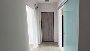 Un couloir avec une porte en bois, une porte en verre et un luminaire au plafond.