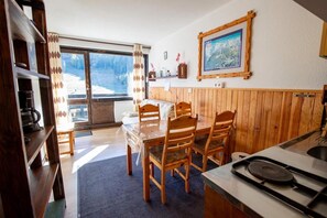 A kitchen with wooden cabinets, a dining table with chairs, a stove, and a large window with curtains. - 250m from ski slopes, 2nd floor, balcony, tv, 23m², La Norma (La Norma)
