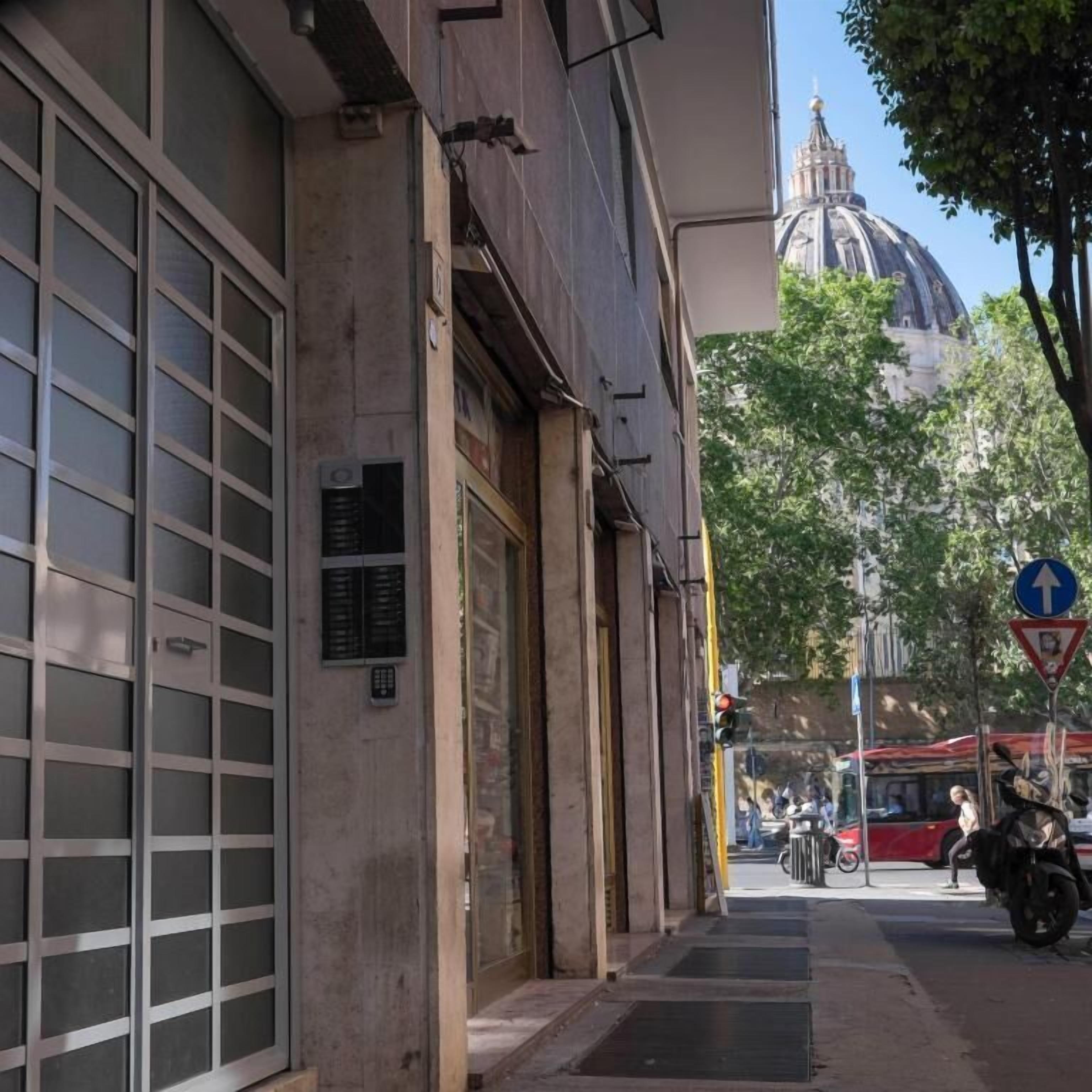 Une vue de rue avec un immeuble doté de grandes fenêtres et d’une porte, un autobus rouge en arrière-plan et un panneau de signalisation.