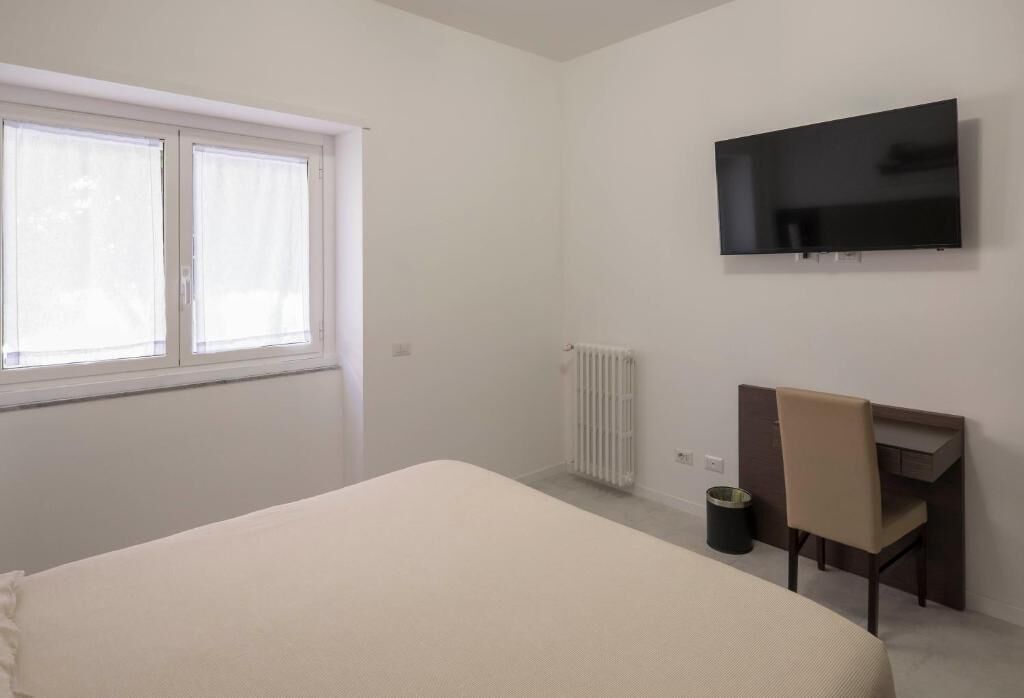 Een kamer met een bed, een bureau, een stoel, een radiator, een televisie en een raam.