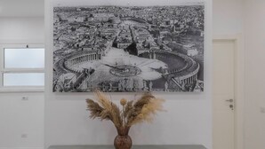 Ein modernes Zimmer mit einem großen schwarz-weißen Stadtbild an der Wand, einer Holzkommode mit einer Vase getrockneter Pampasgräser und einer Tür im Hintergrund.