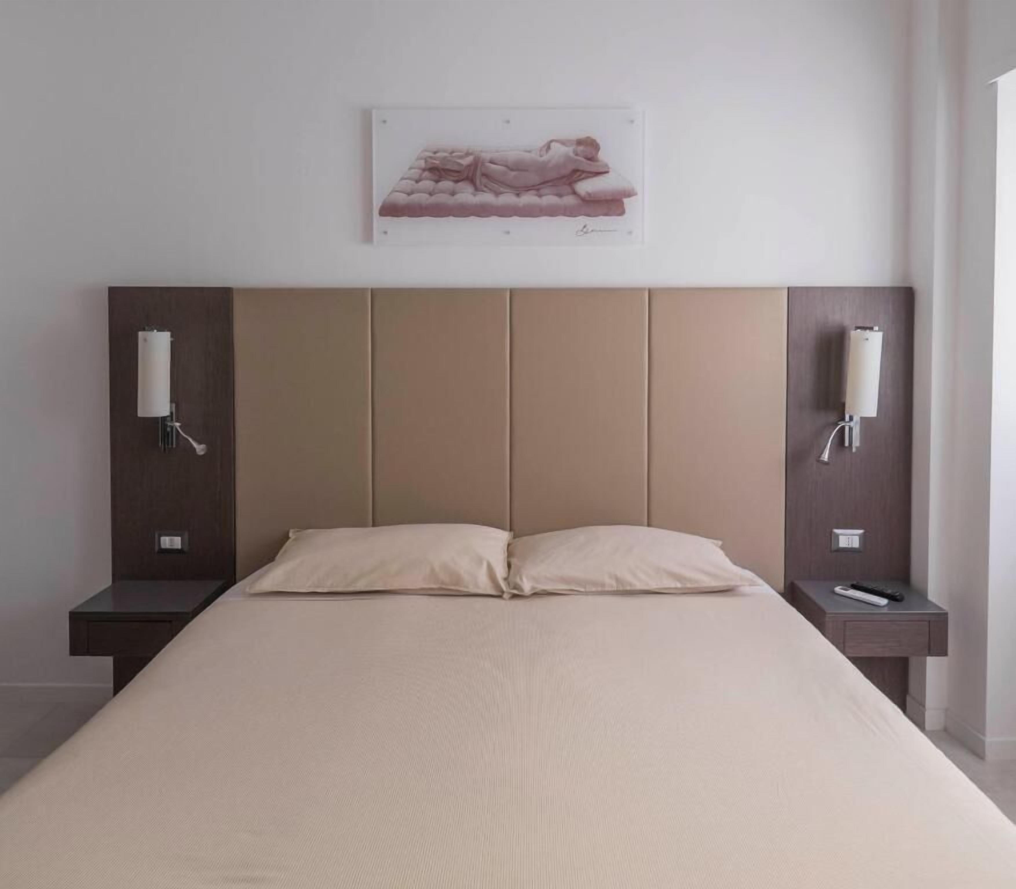Ein Bett mit Kopfteil, zwei Nachttische und ein an der Wand befestigtes Kunstwerk.