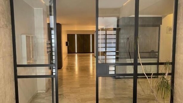 Ein modernes Interieur mit Glastür zu einem Flur, einer Topfpflanze und einem regalartigen Metallgestell.