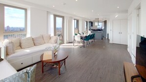 Un'ampia zona giorno con divano, tavolo da pranzo e sedie, una cucina sullo sfondo e grandi finestre con vista sulla città.