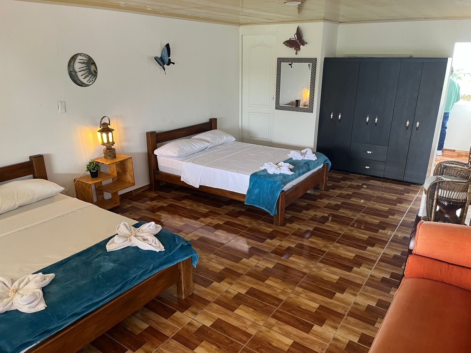 A hotel room with two beds, a wardrobe, a small table with a lamp, and a mirror on the wall.