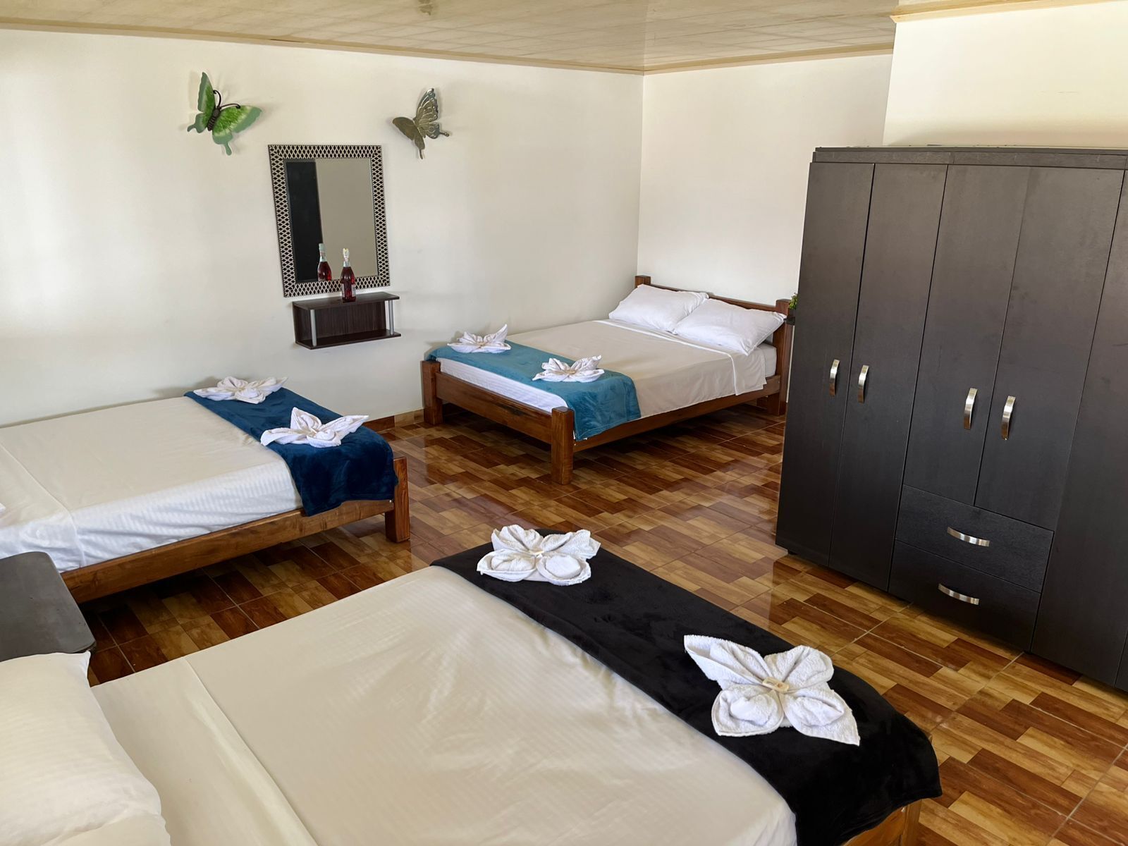 A hotel room with three beds, a wardrobe, a mirror, and decorative butterflies.