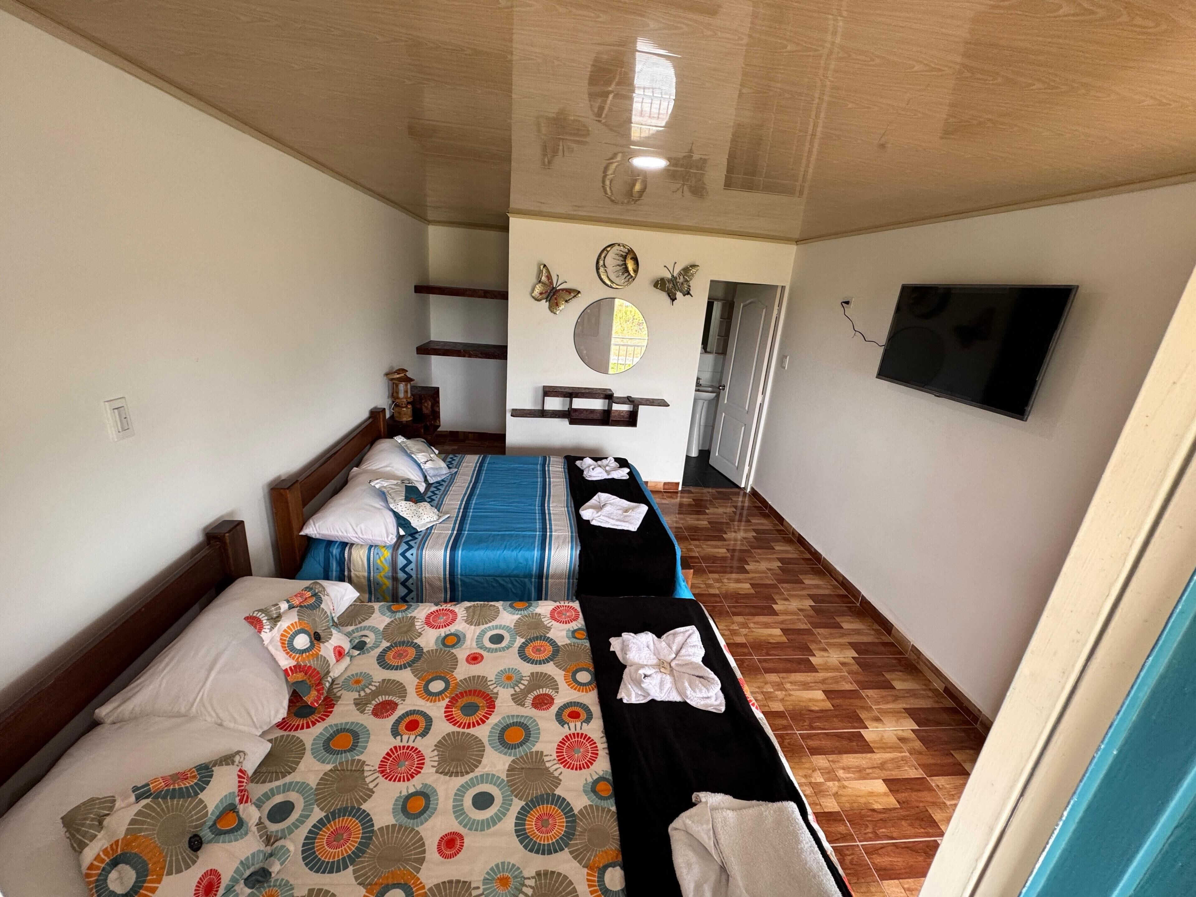 Een hotelkamer met een bed, een tweede bed, een televisie, een spiegel en een houten plafond.