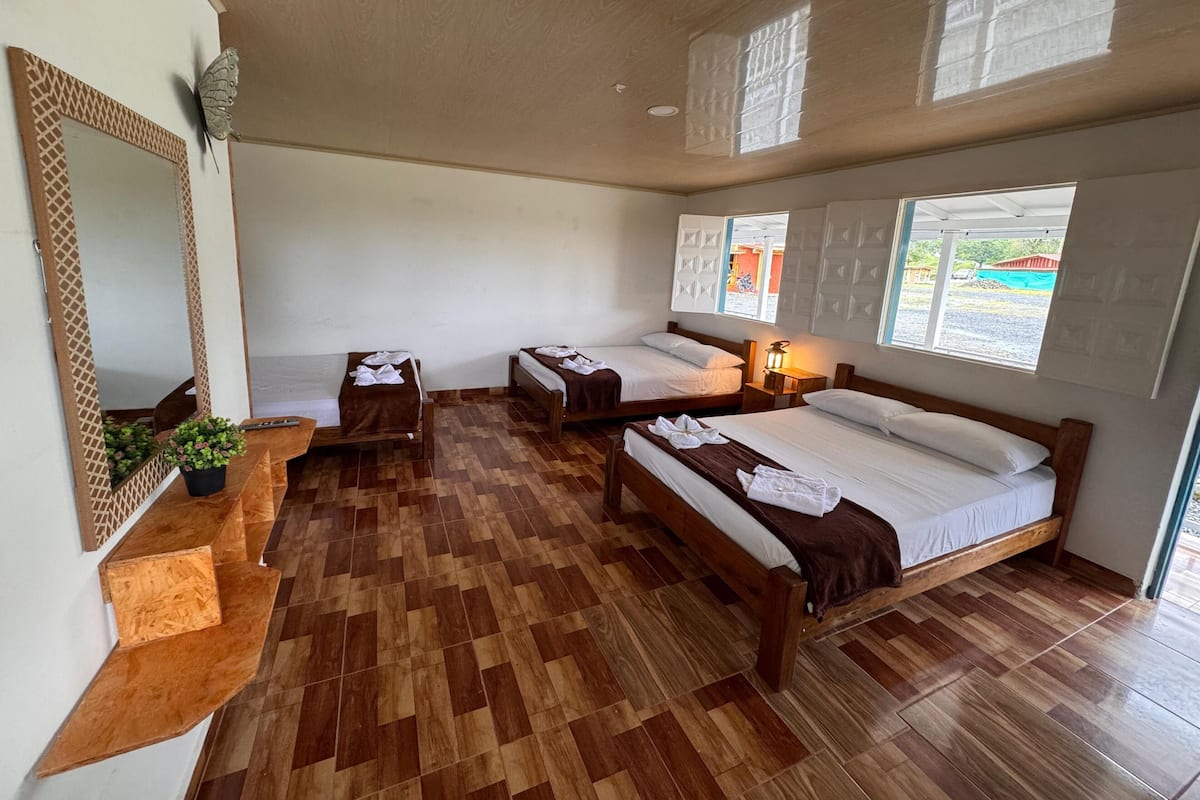 A room with three wooden beds, a wooden bench, a small table, and a mirror.