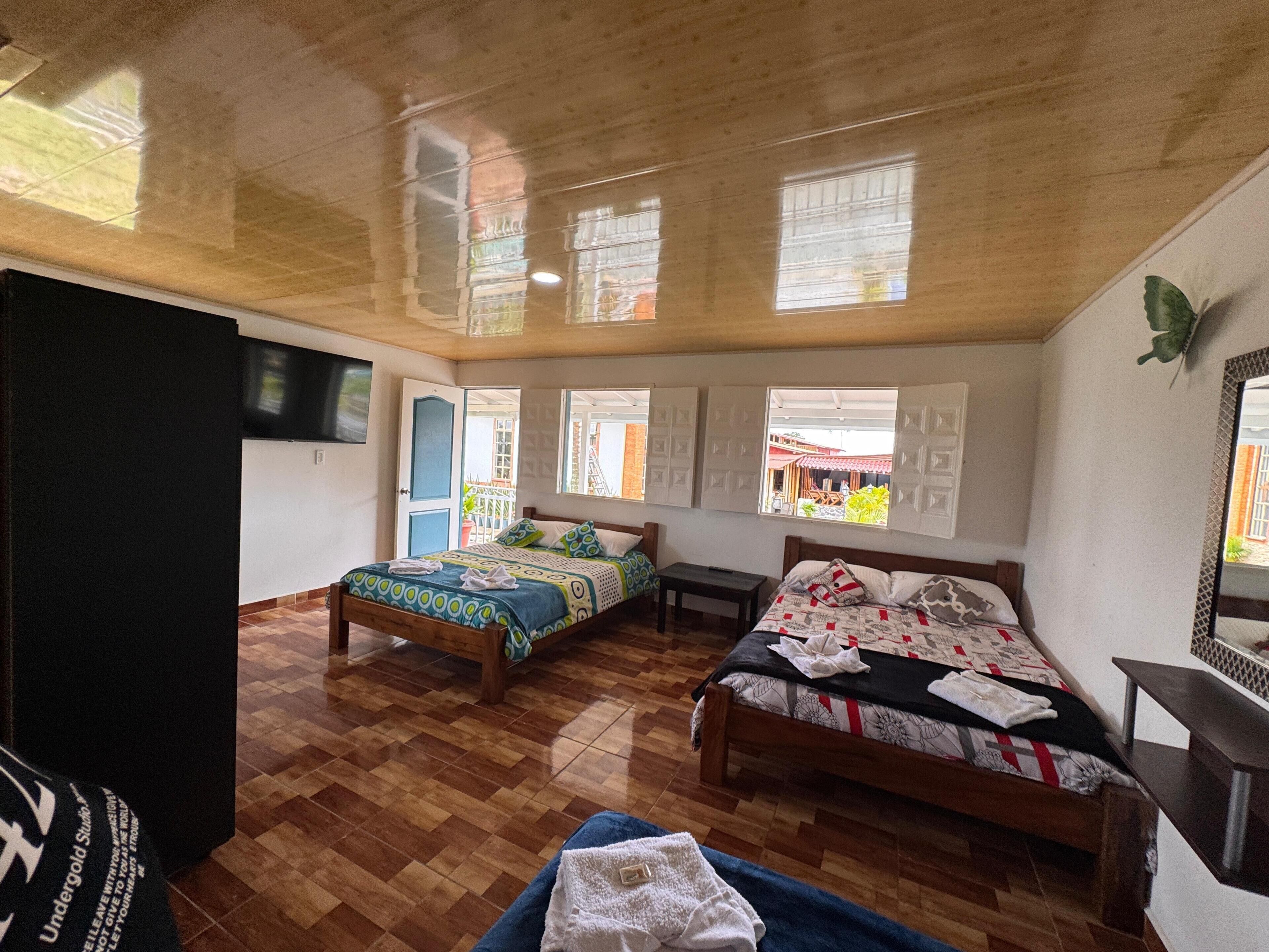 Una habitación con dos camas, techo de madera y ventanas amplias.