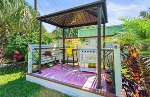A covered outdoor patio with a grill, a white fence, and various plants. - Cozy 2-bedroom house in tranquil New Port Richey with AC (New Port Richey)