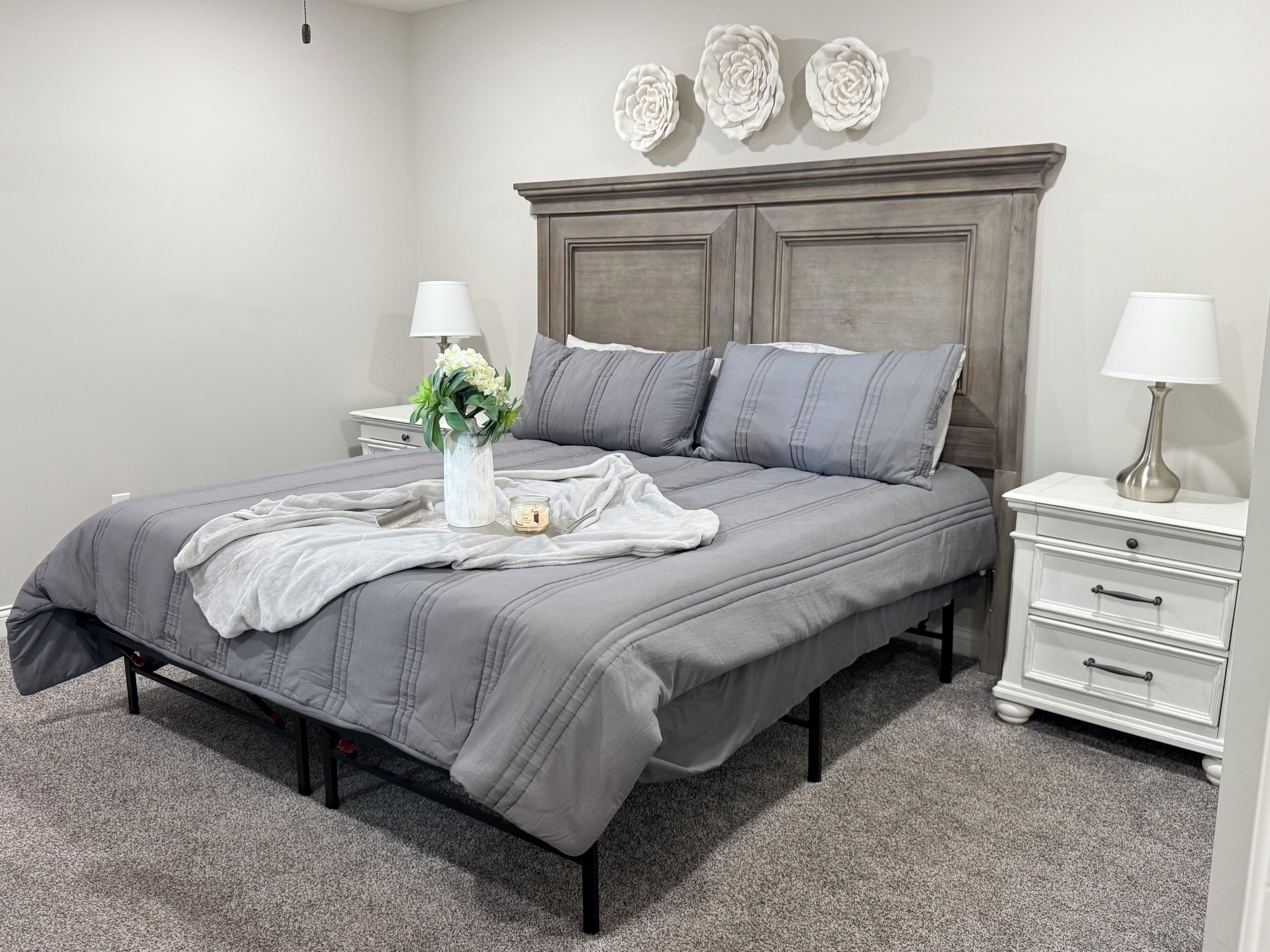 A bedroom with a bed, nightstands, a dresser, a vase with flowers, and wall decorations.