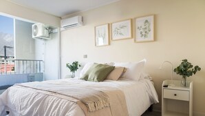 Un dormitorio con cama, mesitas de noche, ventana y balcón.