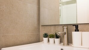 Un baño con un lavamanos blanco, un espejo y un grifo. Hay tres pequeñas macetas con plantas sobre el mostrador del lavamanos.