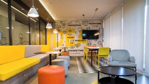 Un espacio de oficina moderno con un sofá amarillo, un reposapiés naranja y una mesa redonda negra.