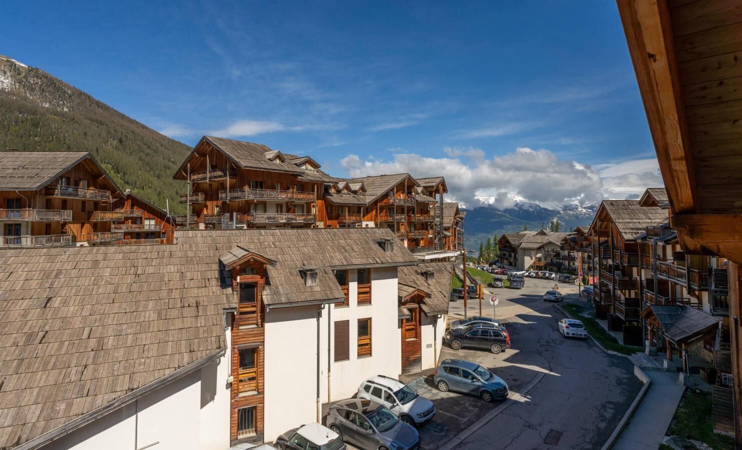 A mountain resort with wooden buildings, balconies, and a view of snow-capped mountains.