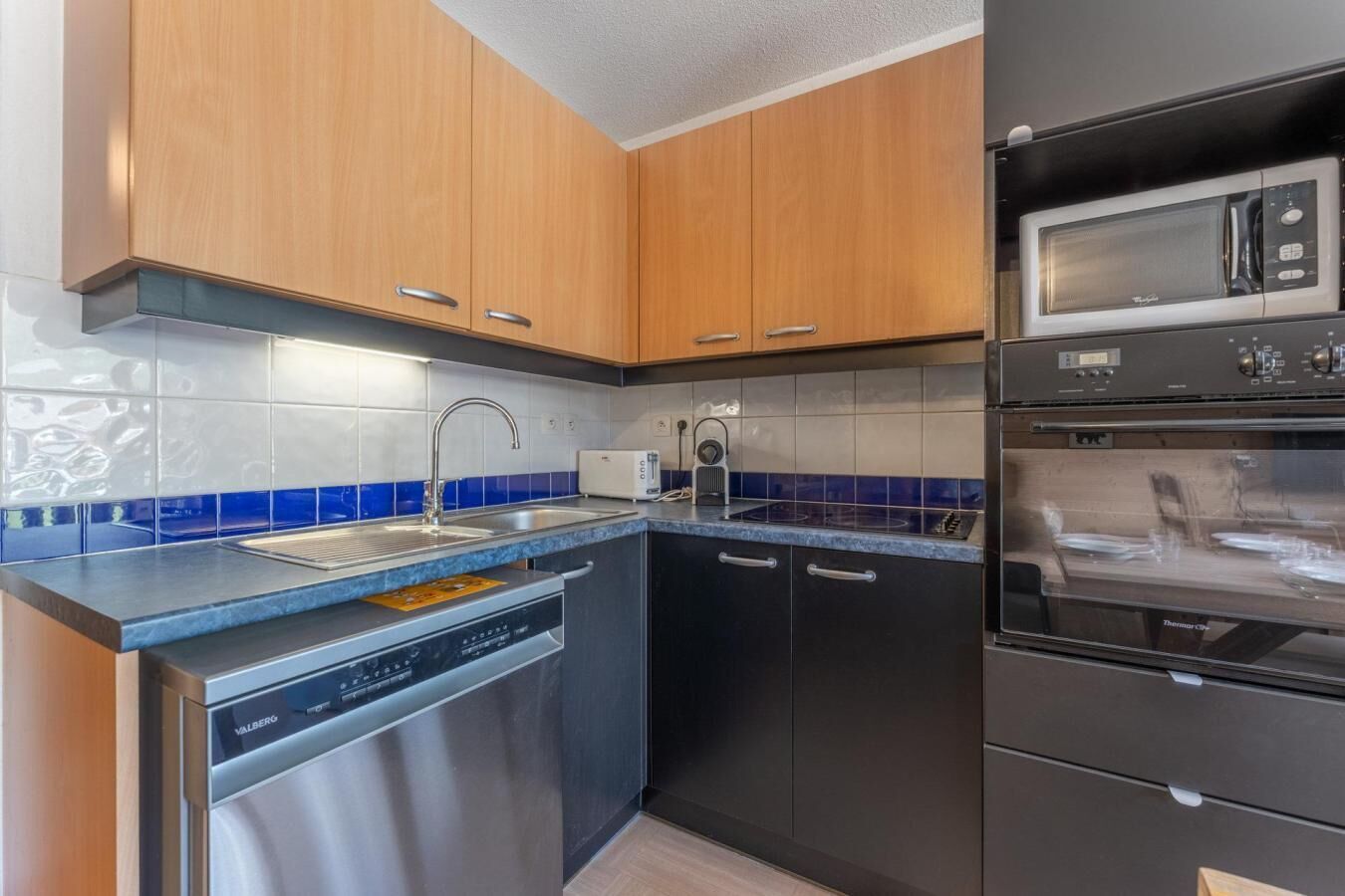 A modern kitchen with wooden cabinets, a dishwasher, a built-in oven, and a microwave.