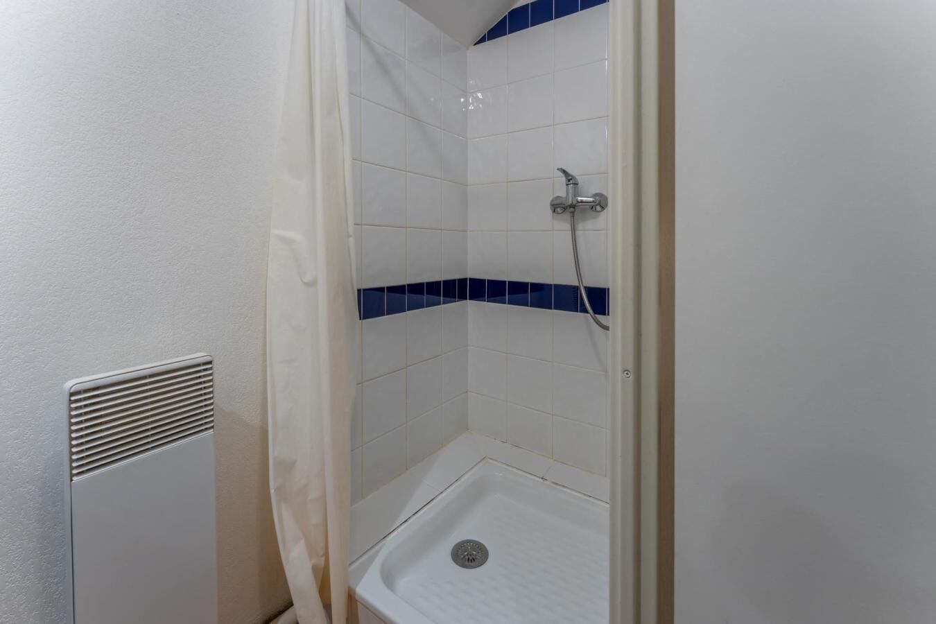 Een douche met een betegelde wand in het wit en blauw, een douchekop en een afvoer.