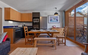 A compact kitchen with modern appliances, a dining area with wooden furniture, and a large sliding glass door to a deck. - 20m from ski lifts, 3rd floor, swimming pool, sauna, balcony, tv, ski locker, 33m², Les Orres (Les Orres)