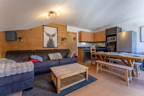 A modern living room with a sofa, a coffee table, and a dining area with a wooden table and benches. - 20m from ski lifts, 3rd floor, swimming pool, sauna, balcony, tv, ski locker, 33m², Les Orres (Les Orres)