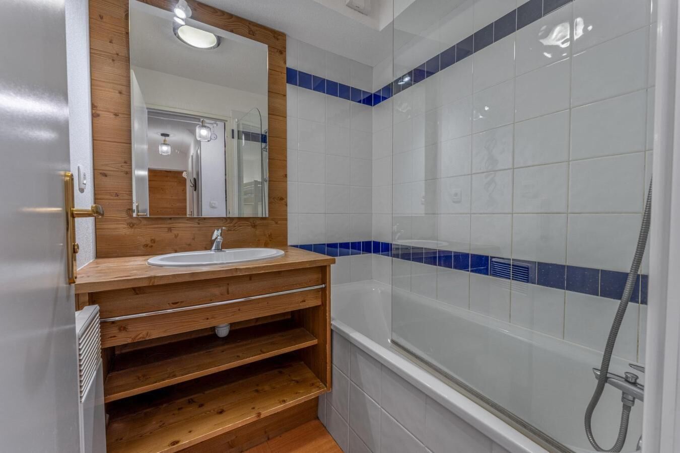 Ein Badezimmer mit einem Holzbadezimmerhocker, einem Spiegel, einem Waschbecken und einer Duschkabine.