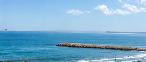Una playa con una torre de salvavidas, sombrillas y un rompeolas rocoso.