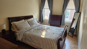 Une chambre à coucher avec un lit, une commode, un miroir et une fenêtre avec des rideaux.