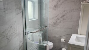 Une salle de bain avec une douche à parois de verre, des toilettes, un lavabo et un sol carrelé en marbre.