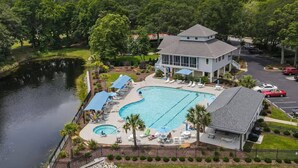 A large swimming pool with lounge chairs and umbrellas, a building with a sloped roof, and a body of water. - Sea Trail Condo with Golf, Pools, Tennis & Beach Access (Sunset Beach)