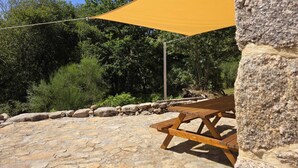A stone patio with a wooden picnic table and a yellow shade sail. - Coração de Dorna House | Castro Laboreiro | Peneda-Gerês National Park (Castro Laboreiro)