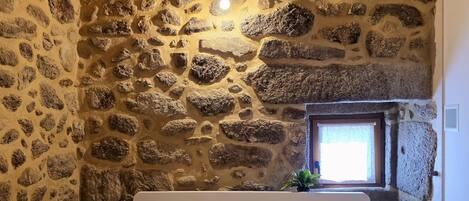 Un dormitorio con pared de piedra, cama con ropa de cama estampada y ventana con vistas.
