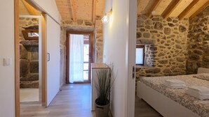 A bedroom with a stone wall, wooden beams, a bed, a nightstand, and a potted plant. - Coração de Dorna House | Castro Laboreiro | Peneda-Gerês National Park (Castro Laboreiro)