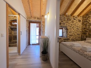 A bedroom with a stone wall, wooden beams, a bed, a nightstand, and a potted plant. - Coração de Dorna House | Castro Laboreiro | Peneda-Gerês National Park (Castro Laboreiro)