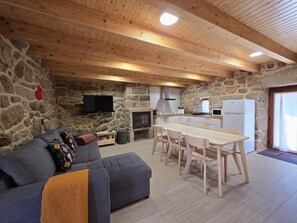 Ein gemütlicher Raum mit Steinwand, Flachbildfernseher, Kamin, Esstisch mit Stühlen und einer Couch.