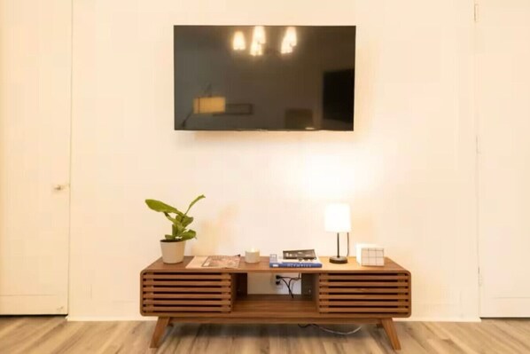 A modern room with a wooden console table, a potted plant, a lamp, and a flat-screen TV mounted on the wall.