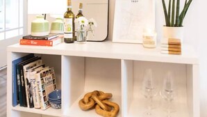 Una estantería ordenada con libros, botellas de vino, un espejo, un cuadro enmarcado, una planta en maceta y cristalería.