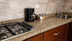 Une cuisine équipée d’une cuisinière à gaz, d’une machine à café, d’un évier et de meubles de rangement en bois.