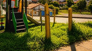 Une aire de jeux avec un toboggan et des structures d’escalade, entourée d’une clôture en treillis métallique et d’une zone herbeuse.