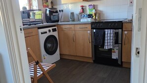 A compact kitchen with a washing machine, oven, and wooden cabinets. - Spacious 2 bedroom maisonette (Broughton)