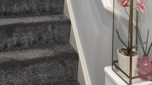 A staircase with a handrail, a framed picture on the wall, and a glass terrarium with flowers on a white console table. - Spacious 2 bedroom maisonette (Broughton)